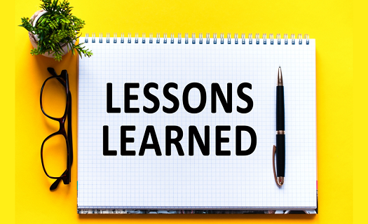 A yellow desk with a notebook and other implements on its surface. The notebook says LESSONS LEARNED in large print.