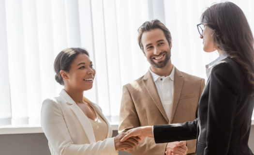 Three people in business attire greeting one another in a sunny room.